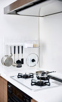 White Grid Panel Organizer next to the stove with utensils, lids and spices on hooks and shelving accessories