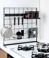 Alternate view of Black Grid Panel Organizer next to the stove with utensils, lids and spices on hooks and shelving attachments